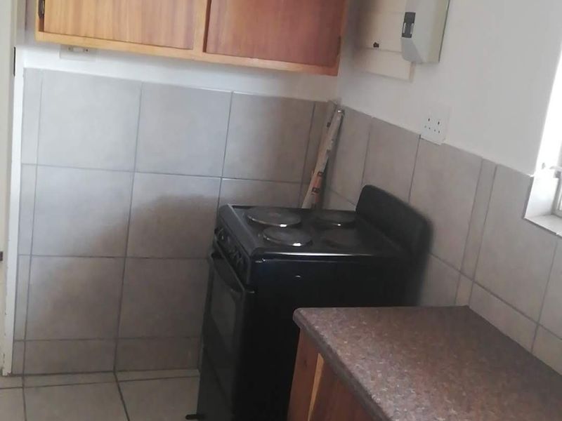 A compact kitchen featuring wooden cabinetry, tiled splashbacks, and a freestanding electric stove.