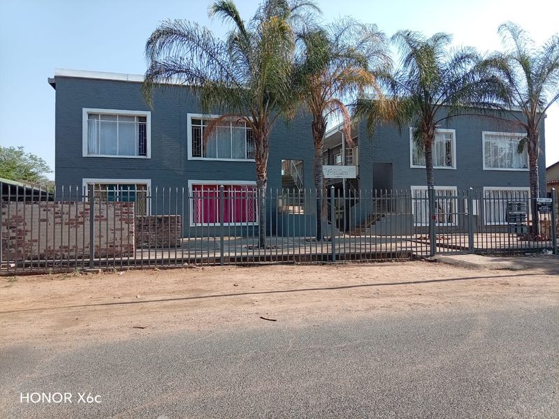 Exterior view of a two-story apartment complex featuring painted brick facade, metal security fencing, and established palm trees.