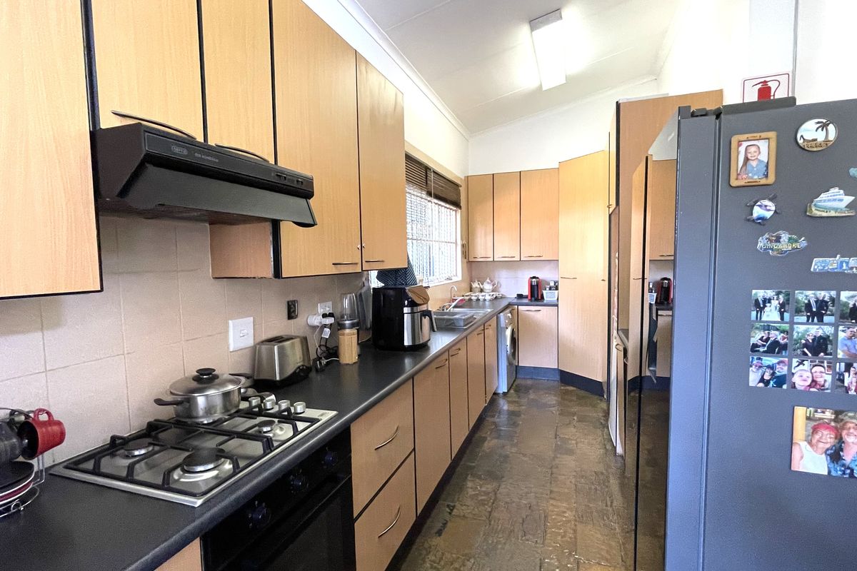 A functional kitchen featuring light wood-tone cabinetry, a gas hob with extractor fan, and stone-style flooring in a practical galley layout.