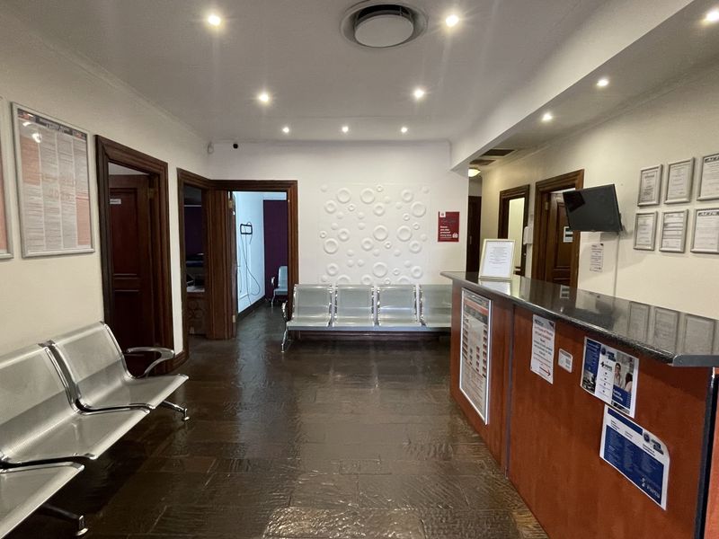 A professional commercial reception area featuring a built-in wooden reception desk, tiled flooring, recessed ceiling lighting, and integrated waiting area seating.