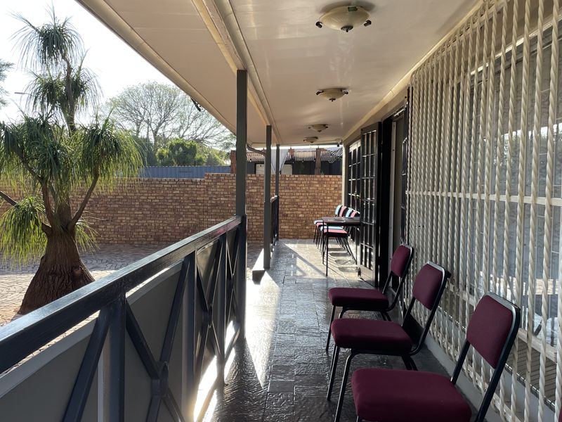 A covered outdoor patio area featuring tiled flooring, metal security gates, and a view of the paved courtyard and brick boundary wall.