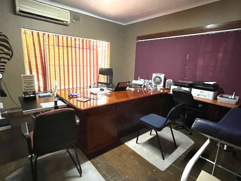 A functional commercial office space featuring a built-in air conditioning unit, vertical blinds, and wood-look flooring.