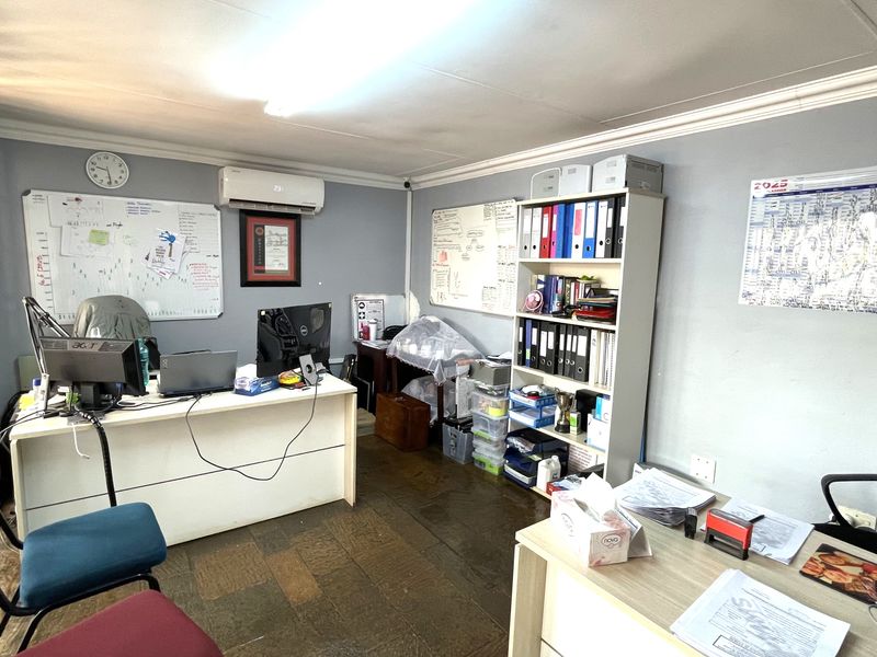 A functional commercial office space featuring tiled flooring, wall-mounted air conditioning unit, and ample wall space for whiteboards and organizational displays.