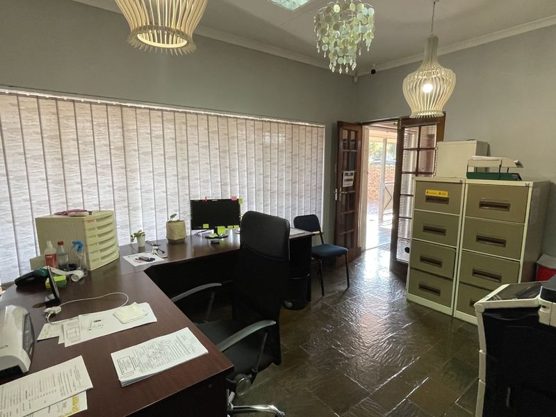 A functional commercial office space featuring tiled flooring, vertical window blinds, and direct access to an outdoor area.