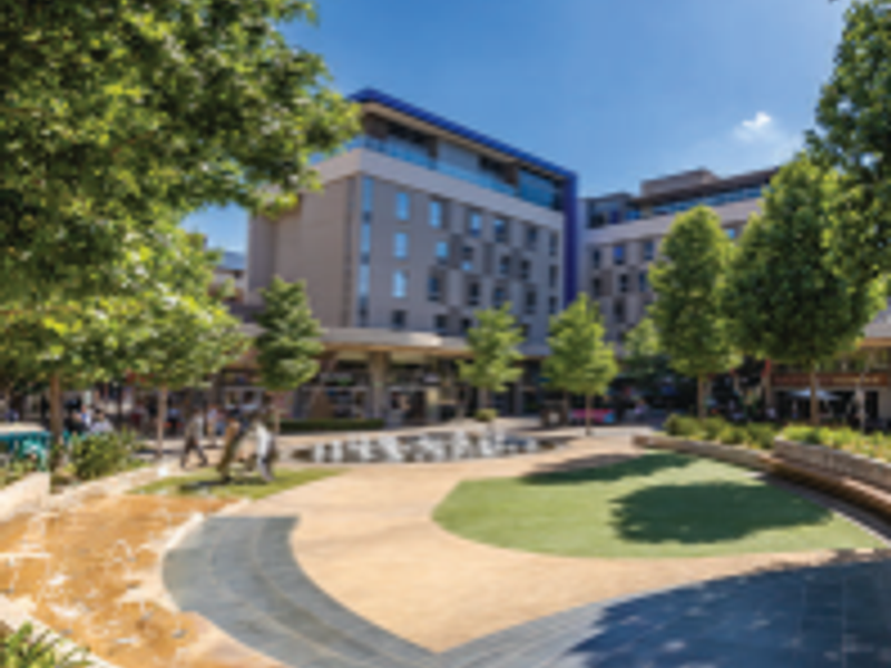 A well-maintained office complex courtyard featuring landscaped gardens, a central water feature, and paved walkways between multi-story commercial buildings.