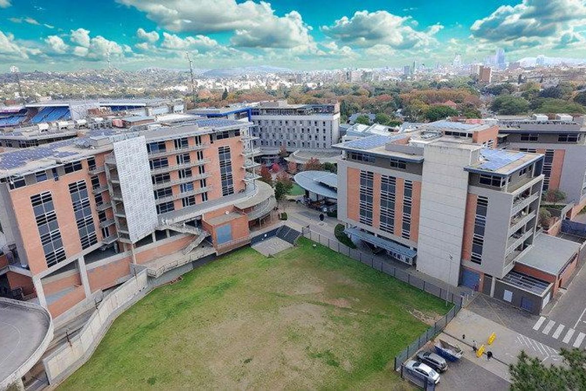 Aerial view of a modern multi-story office complex featuring brick facades, solar panel installations, and surrounding landscaped grounds with paved access.
