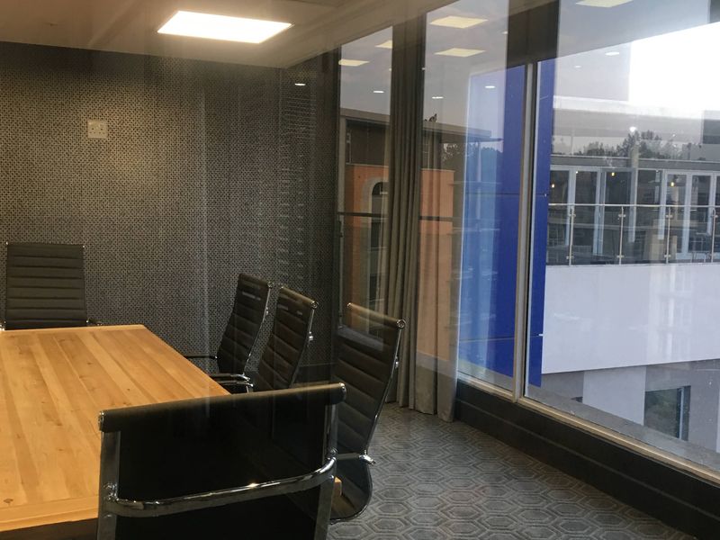 A modern office meeting room featuring floor-to-ceiling windows, recessed lighting, and a textured feature wall, providing a professional workspace environment.