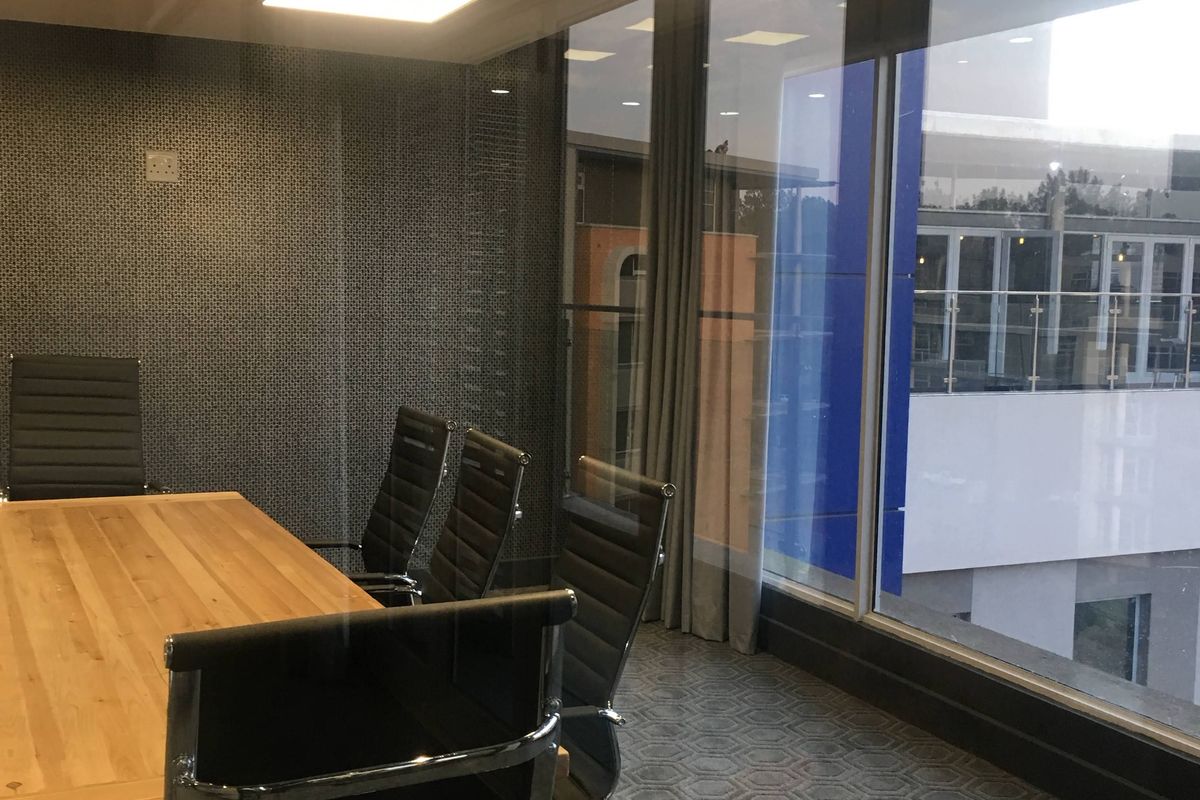 A modern office meeting room featuring floor-to-ceiling windows, recessed lighting, and a textured feature wall, providing a professional workspace environment.