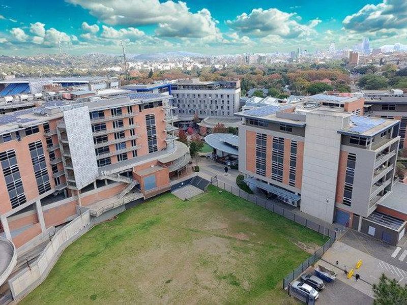 Aerial view of a modern multi-story office complex featuring brick facades, solar panel installations, and surrounding landscaped grounds with paved access.