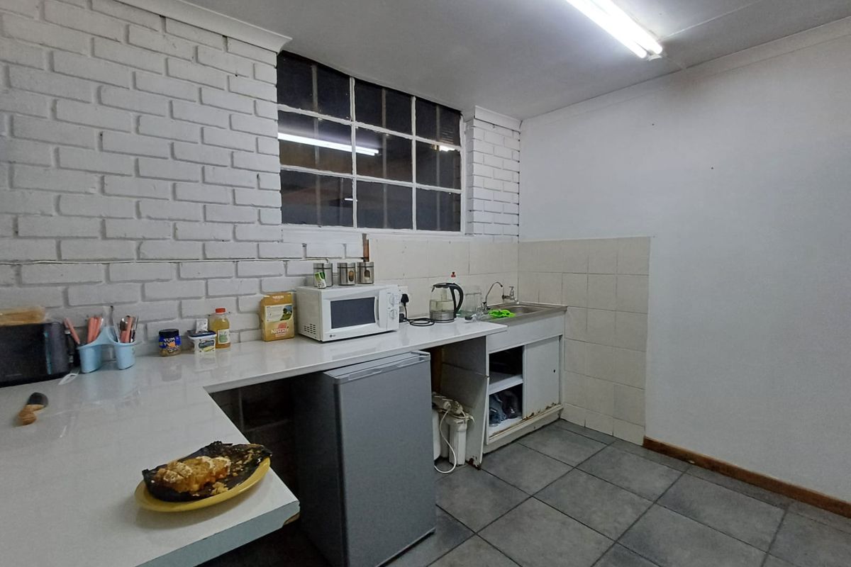 A functional kitchenette area featuring a sink, tiled splashback, white brick wall finish, and tiled flooring.