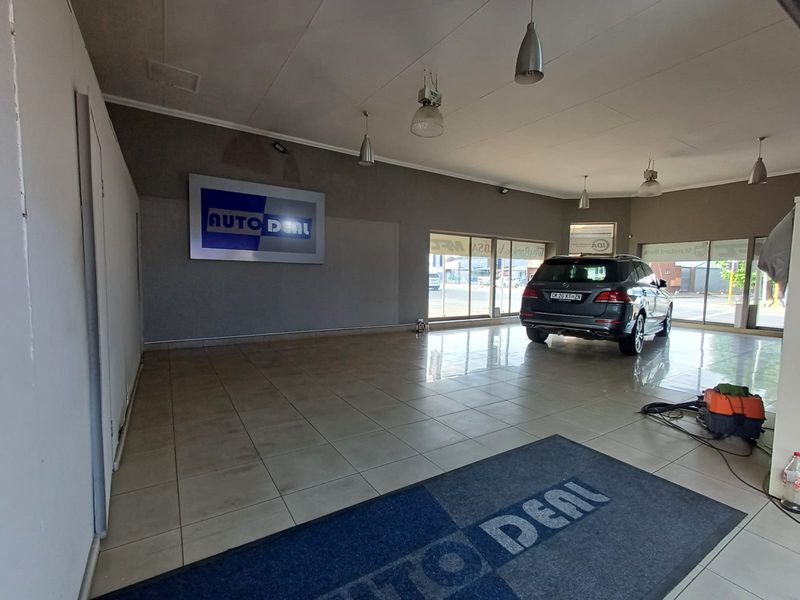 A commercial showroom space featuring tiled flooring, large glass display windows, and modern pendant lighting, suitable for vehicle display or retail use.