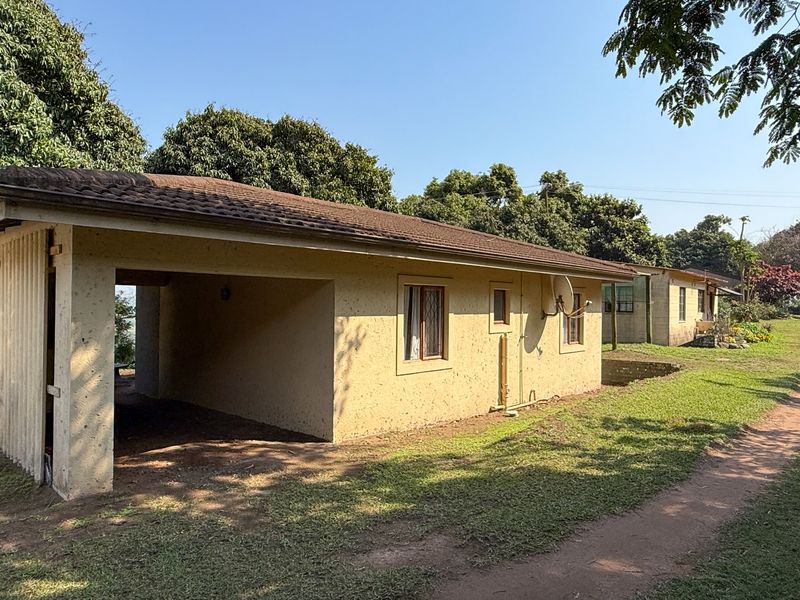 Exterior view of a farm dwelling featuring a covered carport area, tiled roof, and surrounding rural landscape.