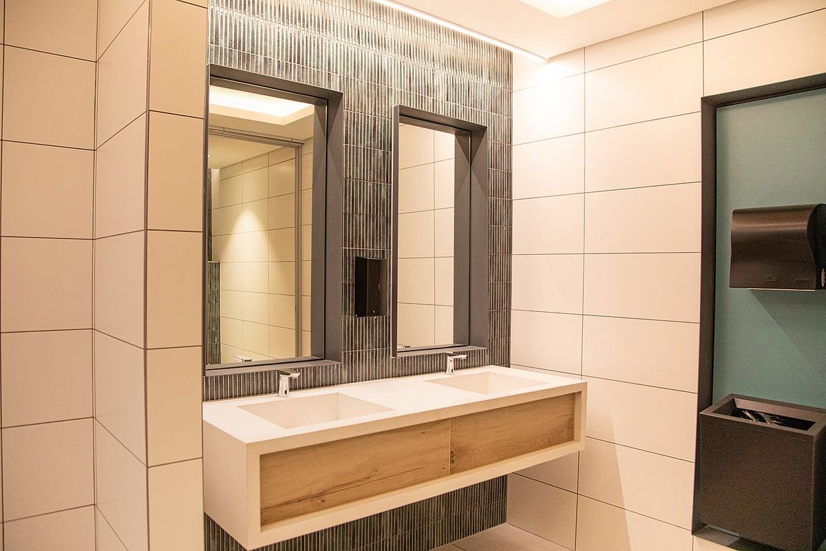 Modern office bathroom featuring a sleek double vanity with integrated sinks, recessed mirrors, and contemporary tiled wall finishes.