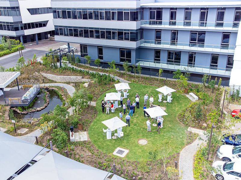 Aerial view of a modern office complex featuring a landscaped garden, water feature, paved walkways, and dedicated parking facilities.