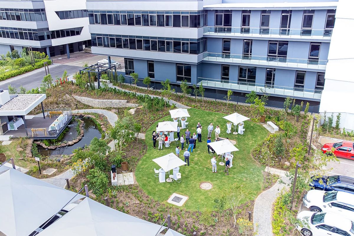 Aerial view of a modern office complex featuring a landscaped garden, water feature, paved walkways, and dedicated parking facilities.