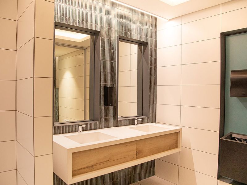 Modern office bathroom featuring a sleek double vanity with integrated sinks, recessed mirrors, and contemporary tiled wall finishes.