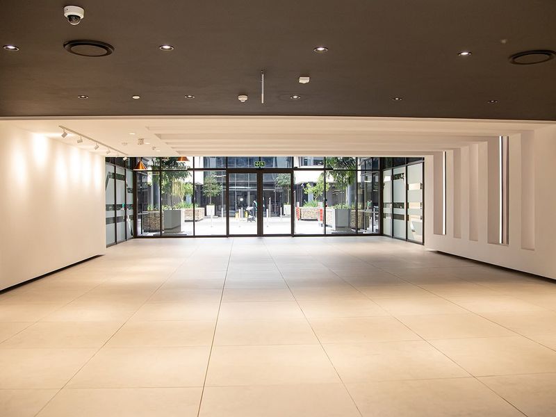A spacious, modern open-plan office area featuring large glass windows, neutral ceramic tiling, and recessed ceiling lighting, offering a bright and professional workspace.