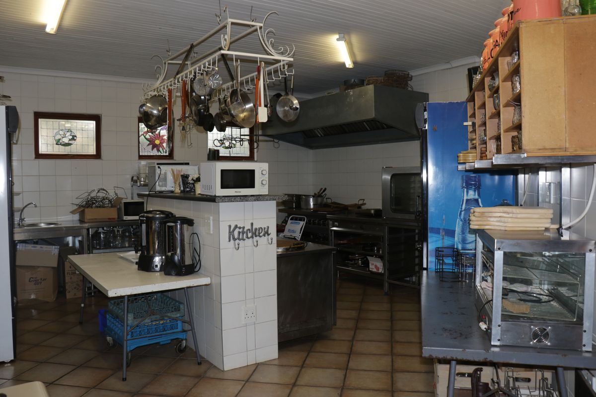 Commercial kitchen featuring stainless steel prep areas, industrial extractor hood, tiled walls, and overhead pot rack storage.