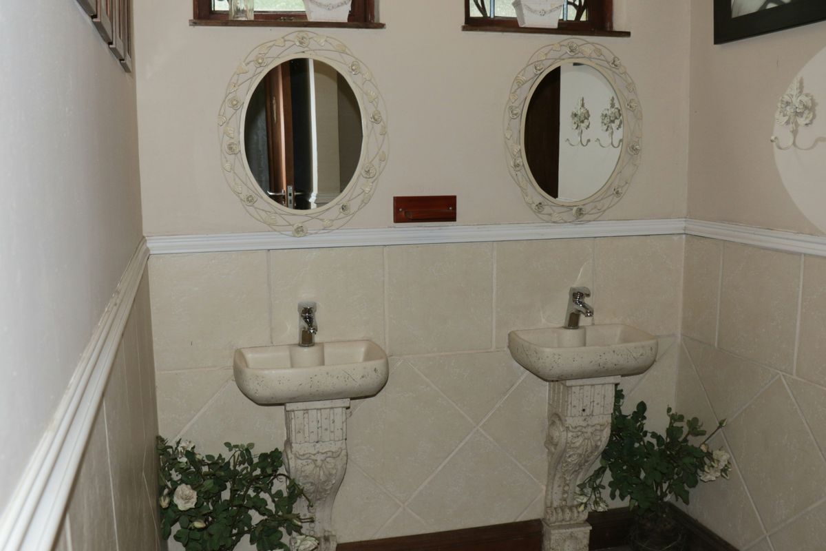 A functional bathroom featuring dual pedestal sinks with decorative mirrors and tiled wall wainscoting.