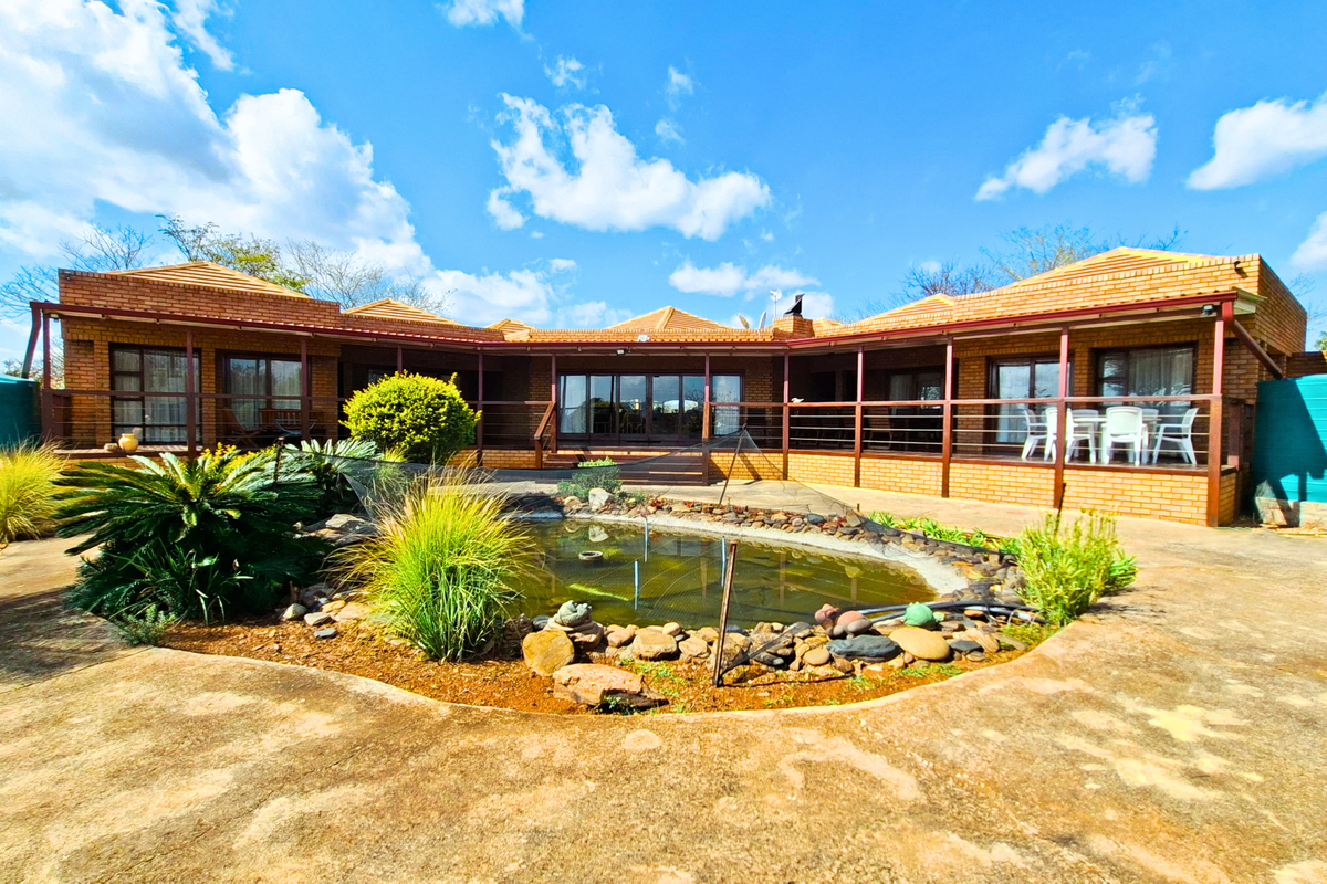 Rear view of a brick-built small holding featuring a covered patio, a central pond, and large water storage tanks set in a landscaped garden.
