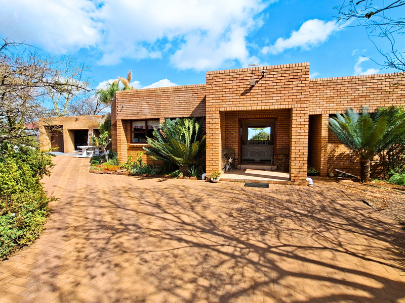 Front elevation of a face-brick small holding featuring a paved driveway, covered entrance, and established garden.