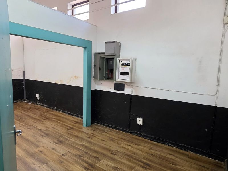 An empty utility or office space featuring laminate flooring, high-level windows, and a wall-mounted electrical distribution board.