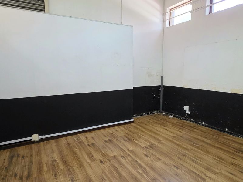 An empty office space featuring laminate flooring, high-level windows, and two-tone wall finishes, requiring minor cosmetic repairs to the wall surfaces.