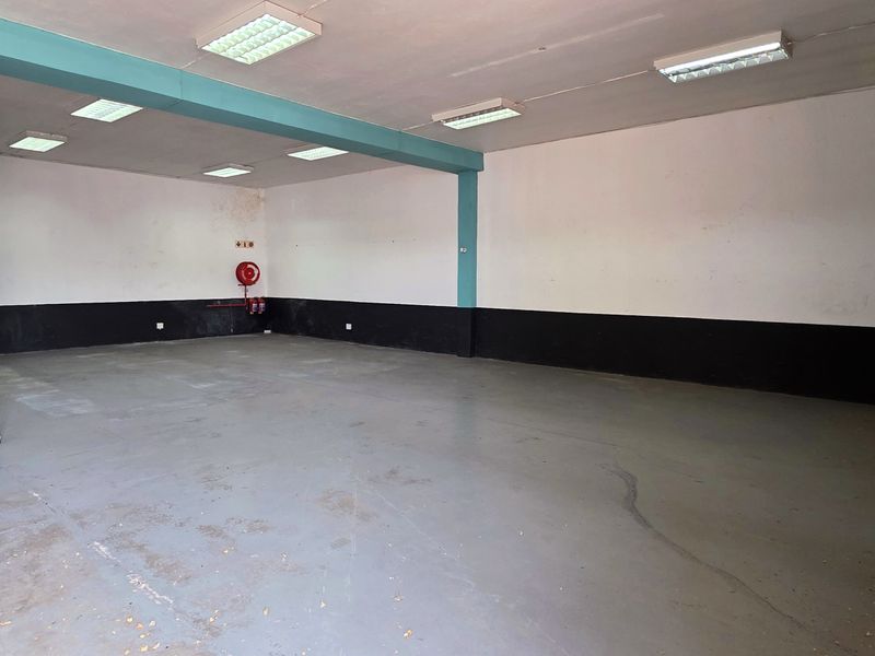 Spacious industrial utility area featuring a painted concrete floor, support columns, fluorescent lighting, and a secure roller shutter door entrance.