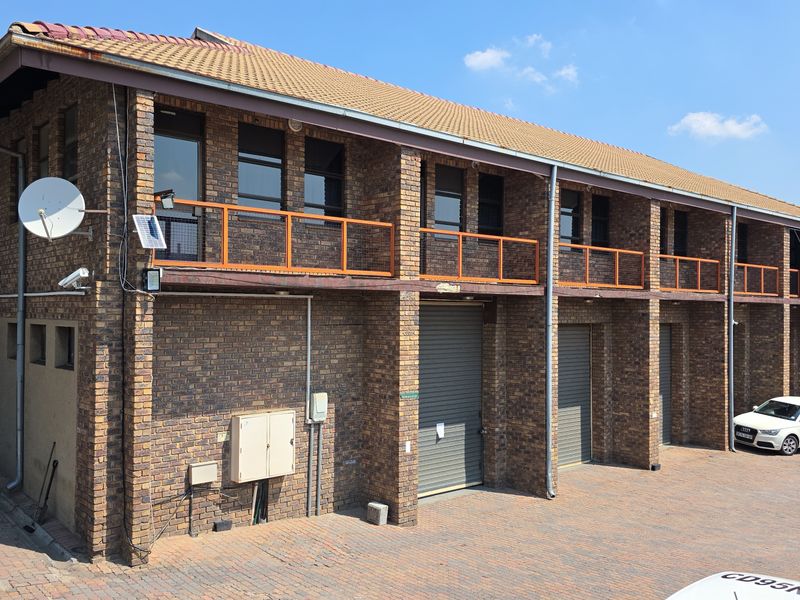 Industrial building featuring a face brick facade, multiple roller shutter doors, and an upper-level balcony with paved driveway access.