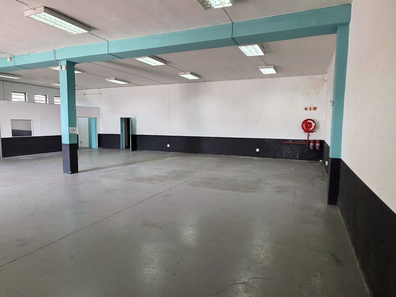 Spacious open-plan industrial unit featuring concrete flooring, fluorescent lighting, and a wall-mounted fire hose reel, suitable for various commercial or industrial applications.