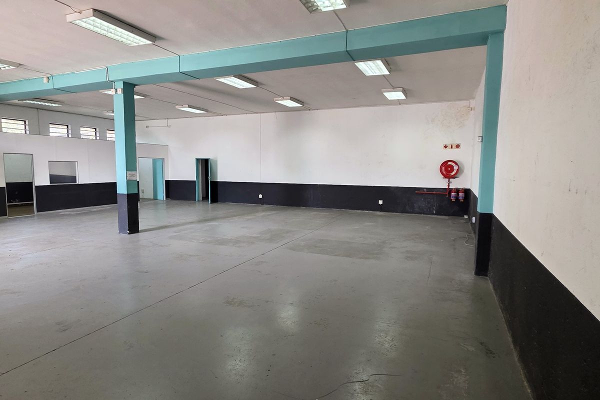 Spacious open-plan industrial unit featuring concrete flooring, fluorescent lighting, and a wall-mounted fire hose reel, suitable for various commercial or industrial applications.