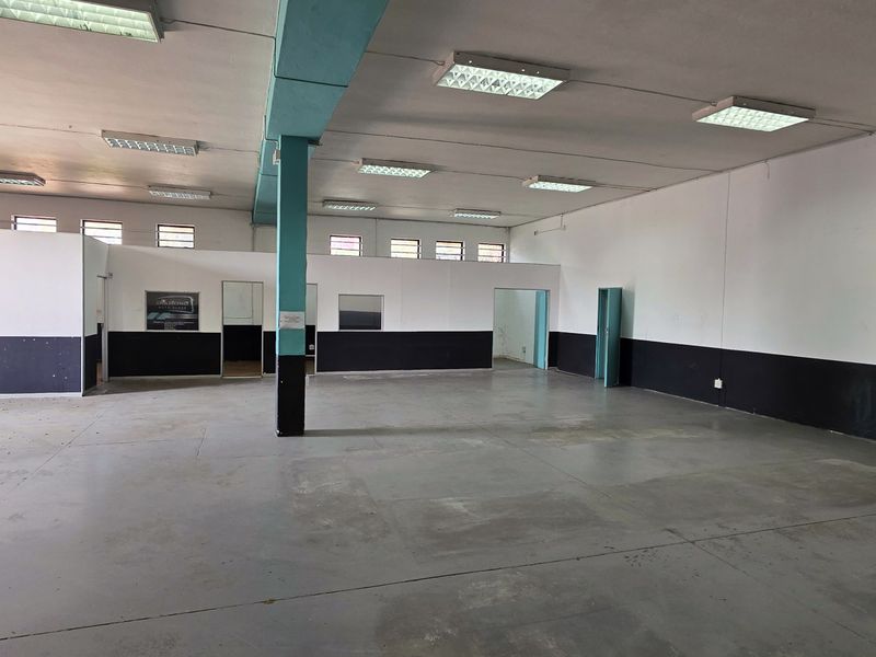 Spacious industrial utility area featuring concrete flooring, fluorescent lighting, and partitioned office space, suitable for workshop or storage use.
