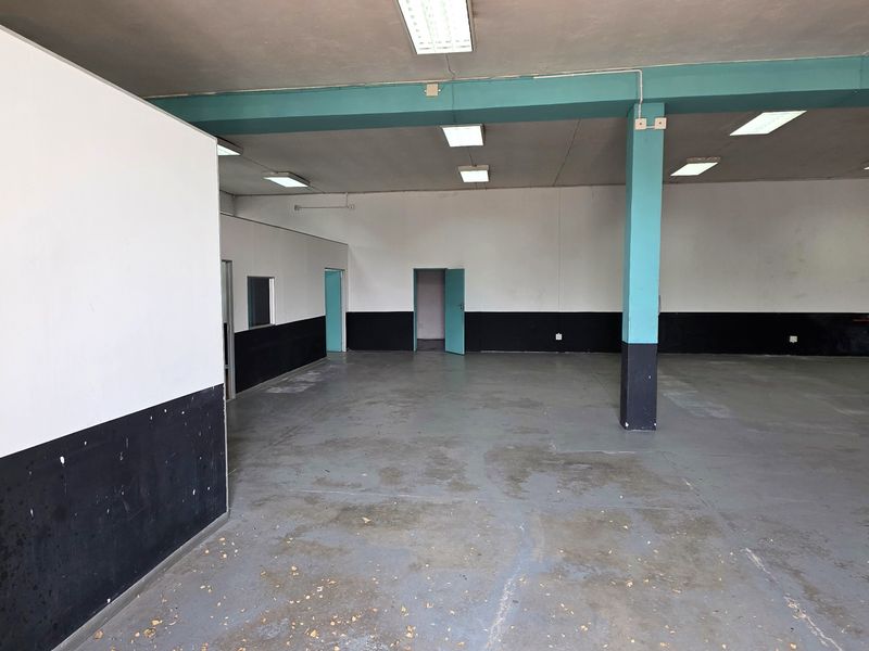 Spacious open-plan industrial unit featuring painted concrete flooring, structural columns, fluorescent lighting, and a wall-mounted fire hose reel.