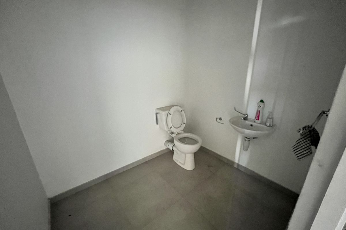 A basic industrial restroom featuring a standard toilet and a wall-mounted hand basin with tiled flooring.