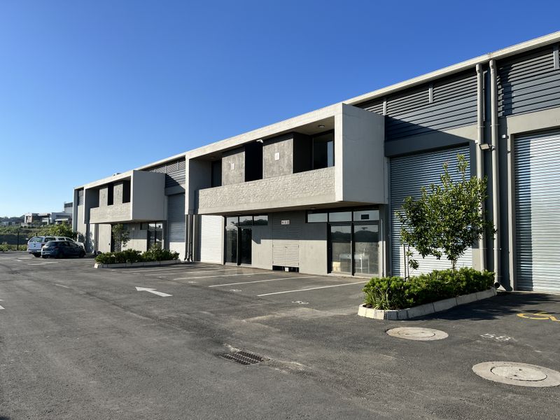 Modern industrial warehouse complex featuring roller shutter doors, concrete facade, and dedicated paved parking bays in a well-maintained business park setting.