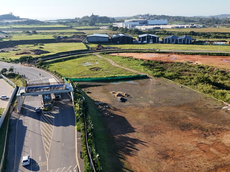 Aerial view of an industrial estate entrance with access control gate, surrounding undeveloped land, and nearby warehouse facilities.