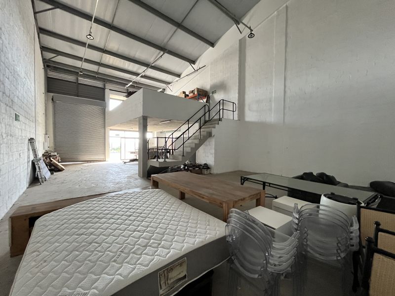 Spacious industrial warehouse unit featuring a high-clearance ceiling, mezzanine level with staircase access, and a large roller shutter door for vehicle access.
