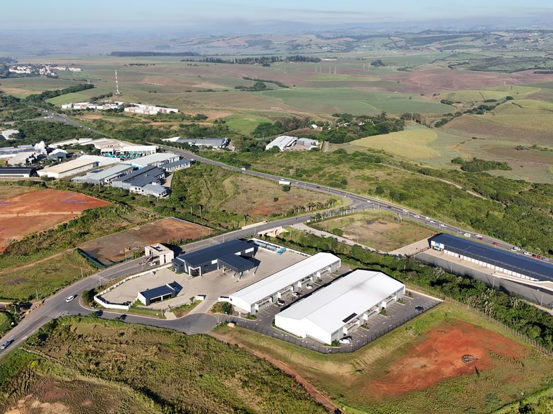 Aerial view of an industrial park featuring multiple warehouse buildings, paved parking areas, and surrounding green landscape with road access.