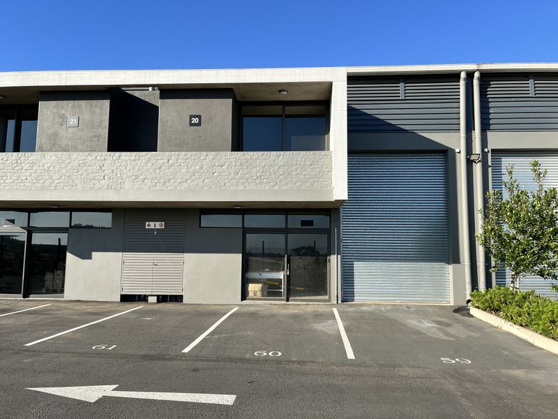 Modern industrial unit featuring a roller shutter door, glass entrance, and dedicated parking bay in a well-maintained commercial complex.