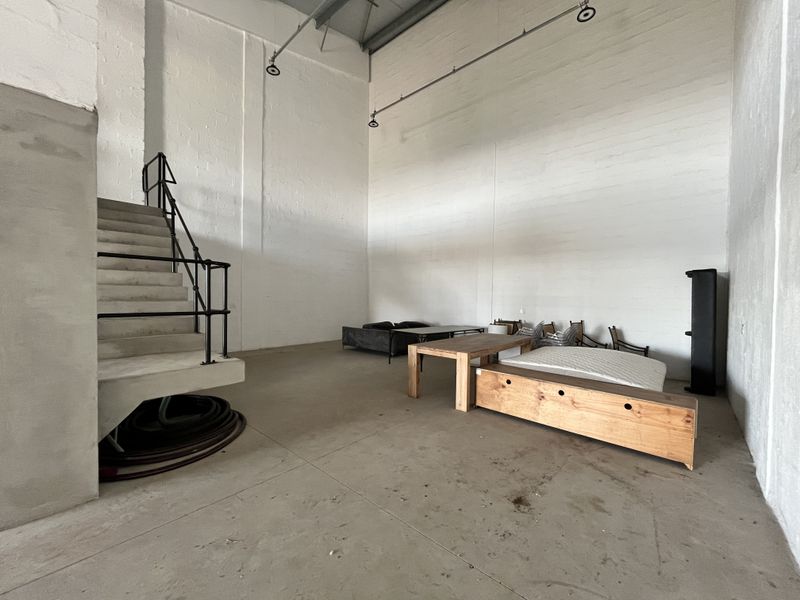 Spacious industrial open-plan area featuring high ceilings, exposed structural elements, and a concrete staircase with metal railing.