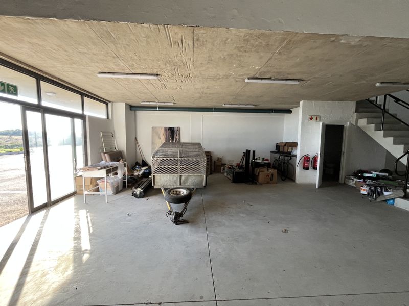Spacious industrial utility area featuring concrete flooring, exposed ceiling, large glass sliding doors for natural light, and an integrated staircase.