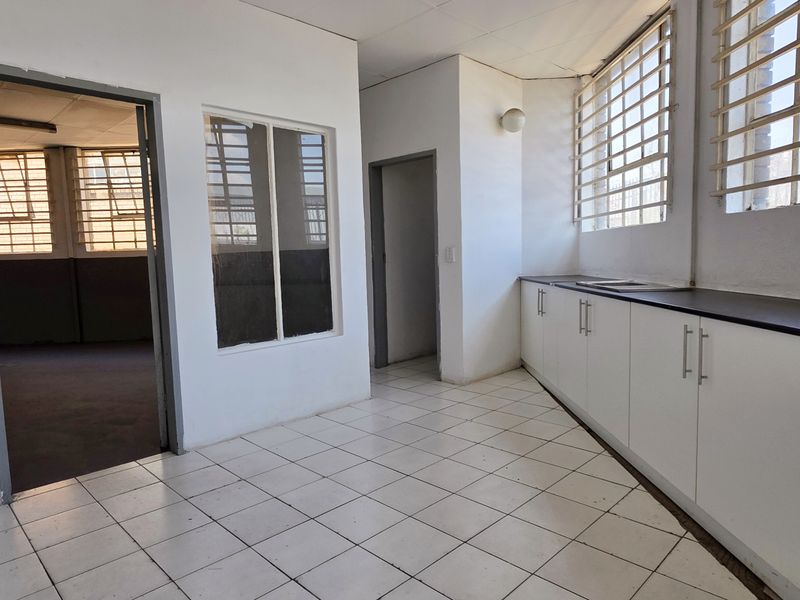 A functional, empty kitchen area featuring built-in cabinetry, a stainless steel sink, and tiled flooring, with security bars installed on the windows.