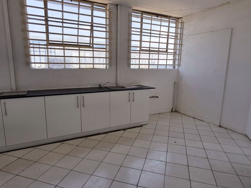 A functional industrial kitchen space featuring white built-in cabinetry, dark countertops, stainless steel sink, and tiled flooring with security bars on the windows.