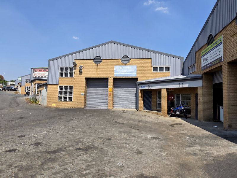 Front elevation of an industrial warehouse complex featuring face brick construction, multiple roller shutter doors, and a paved driveway area.
