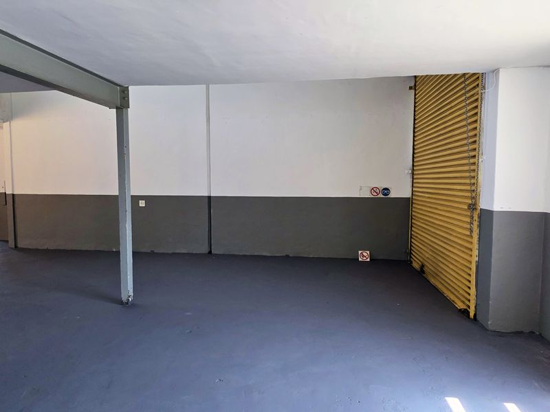 Spacious industrial utility area featuring painted concrete floors, steel support columns, and a secure roller shutter door, suitable for storage or workshop use.