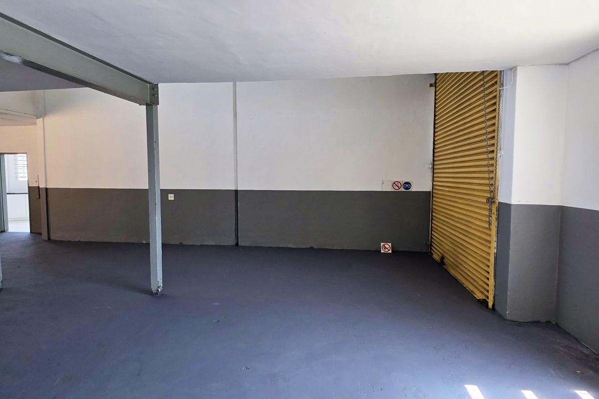 Spacious industrial utility area featuring painted concrete floors, steel support columns, and a secure roller shutter door, suitable for storage or workshop use.