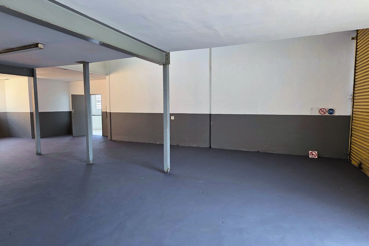 Spacious industrial utility area featuring a large yellow roller shutter door, steel support columns, and durable painted concrete flooring.
