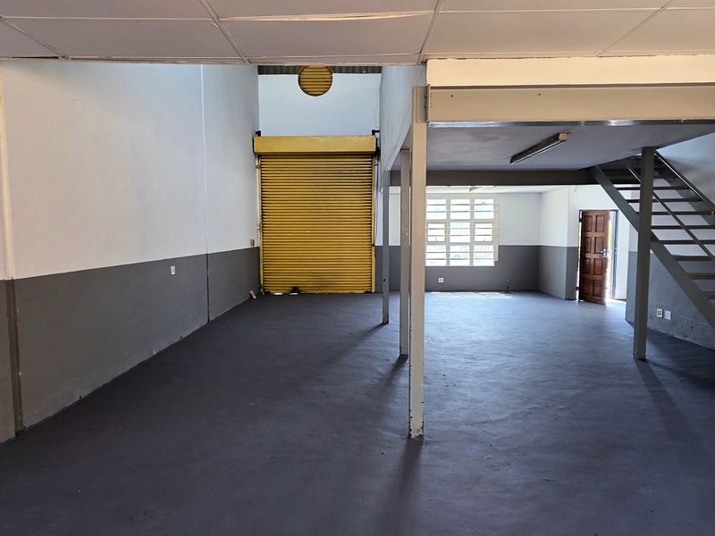 Spacious industrial open-plan unit featuring a mezzanine level, steel staircase, roller shutter door, and durable painted concrete flooring, suitable for various commercial or storage uses.