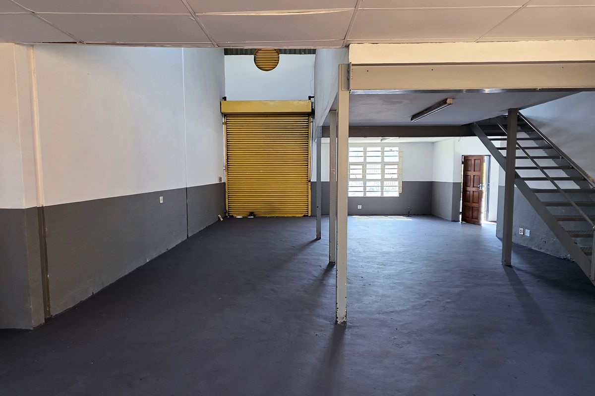 Spacious industrial open-plan unit featuring a mezzanine level, steel staircase, roller shutter door, and durable painted concrete flooring, suitable for various commercial or storage uses.