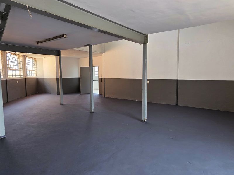 Spacious industrial utility area featuring a steel mezzanine level, staircase, secure window bars, and durable painted concrete flooring, suitable for storage or workshop use.